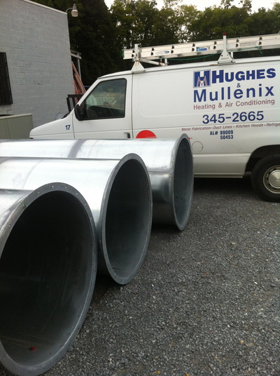 three large metal ducts laying next to Hughes & Mullenix van